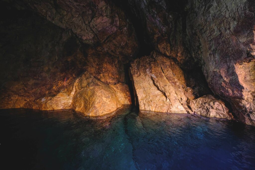 A tranquil natural cave scene featuring eroded rocks reflected in calm water.